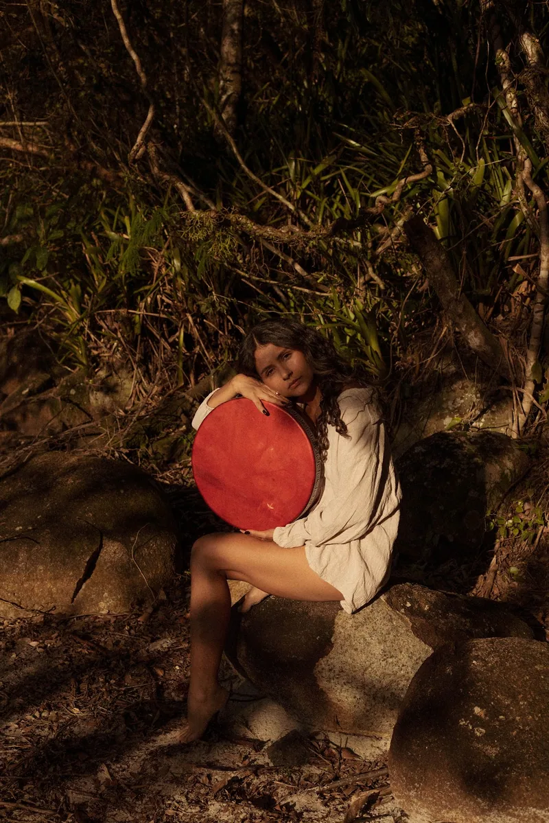 Kalina em ritual com tambor xamânico, sentada entre as rochas do cerrado